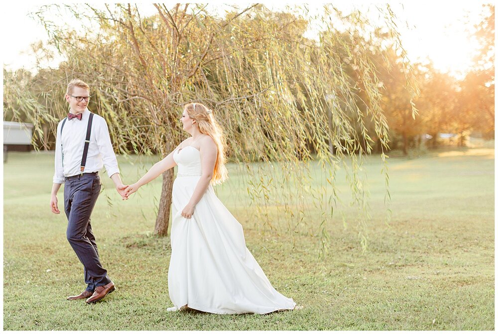 Bailey and Logan walking through a field at golden house after A Holy Family Cathedral Wedding.
