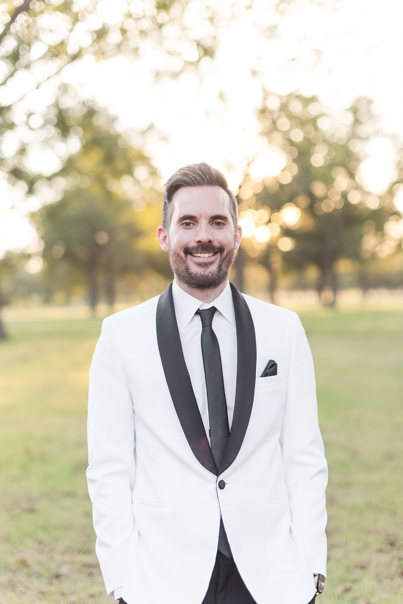 Groom wearing a white tux in a pecan grove at his wedding at Pecandarosa Ranch.