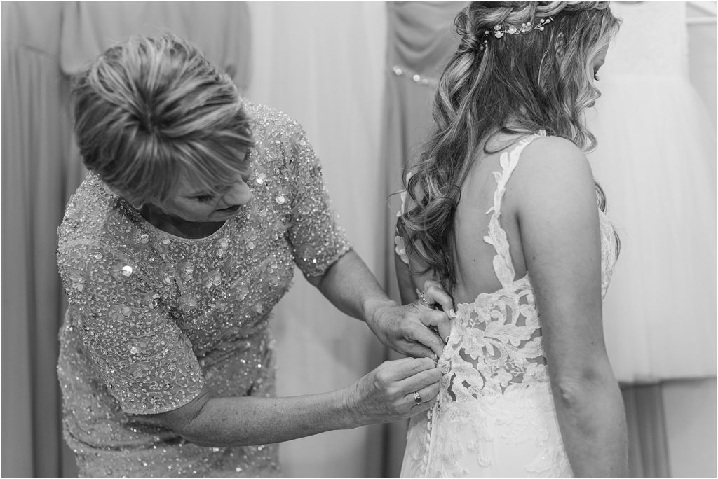A mother helping her daughter button up her lace wedding dress.