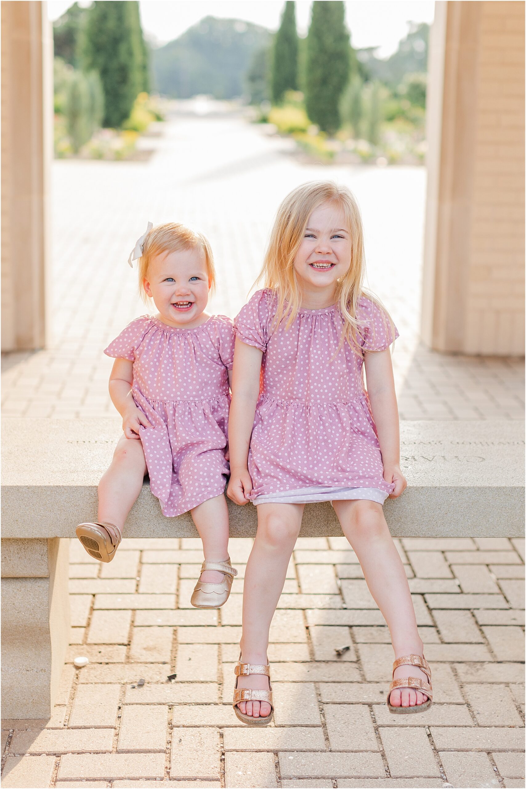 Sisters laughing under the archway at a summer family photo session.