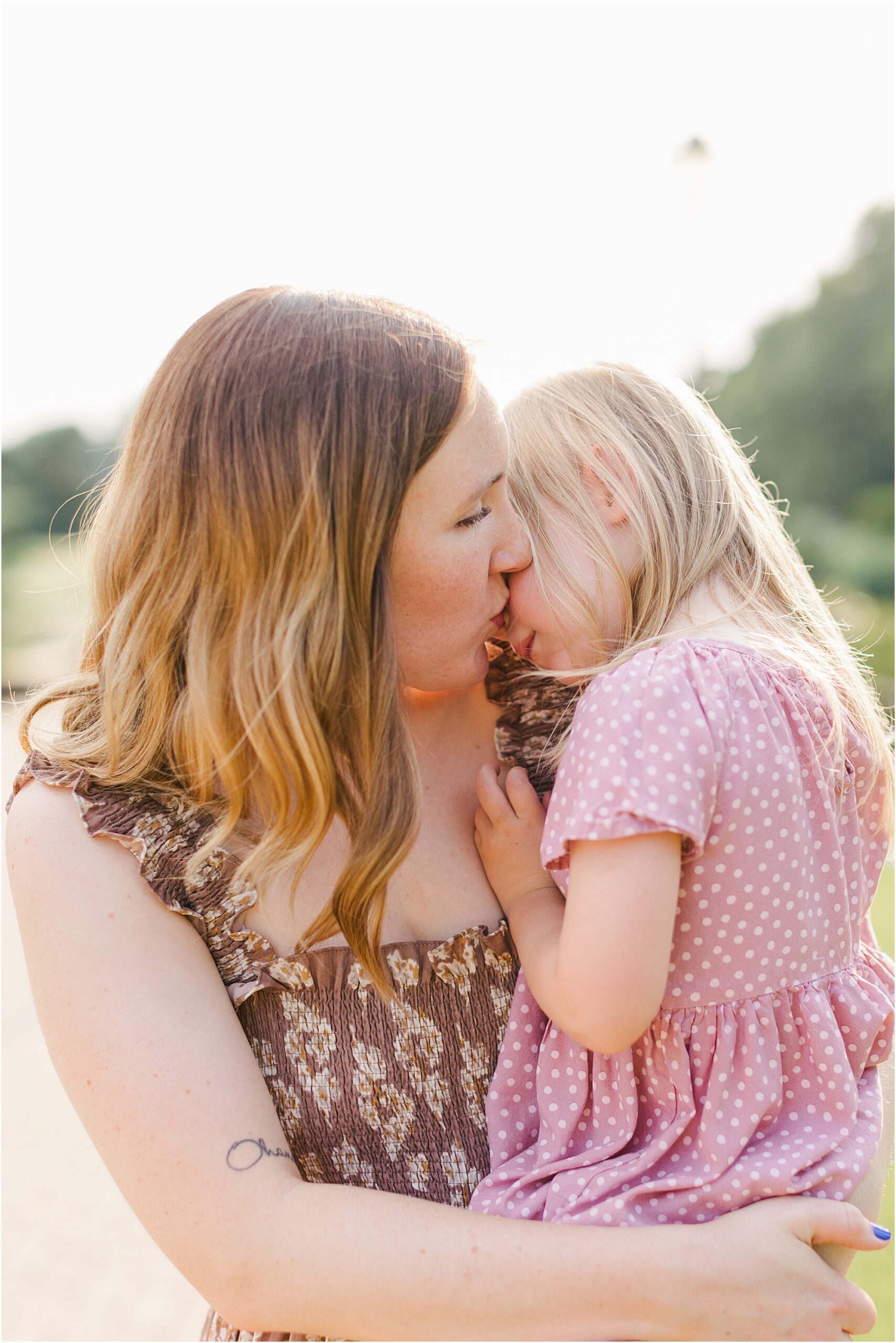Mother kisses her daughter's cheek at their summer family photo session.