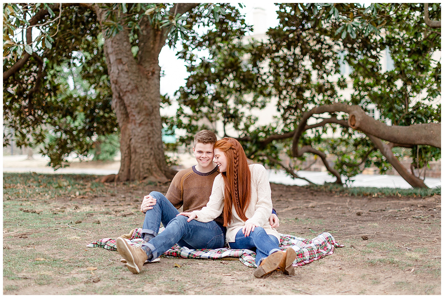 A couple sitting on a blanket in front of a magnolia tree during their engagement session at woodward park.