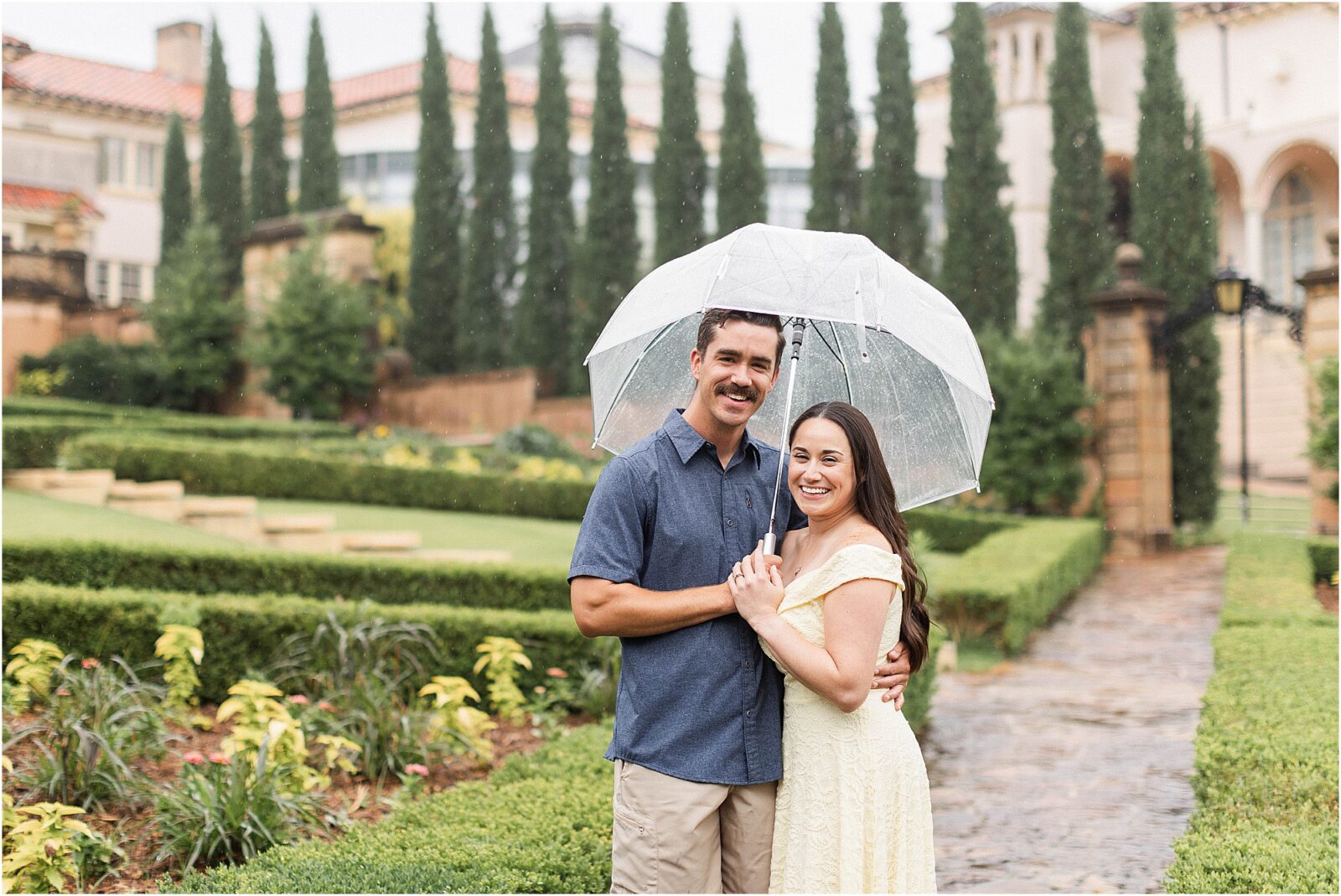 Marie and Mark under an umbrella during a rainy engagement session at the philbrook