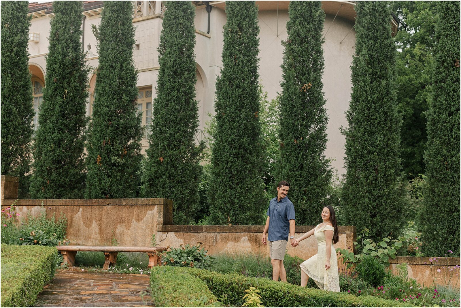 Marie and Mark walking along the Italian spruce trees of the Tuscan inspired gardens during their rainy engagement session at the philbrook museum.
